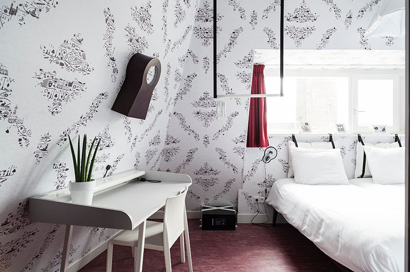 Bright room with a window above a double bed and a desk against the wall | Kaboom Hotel