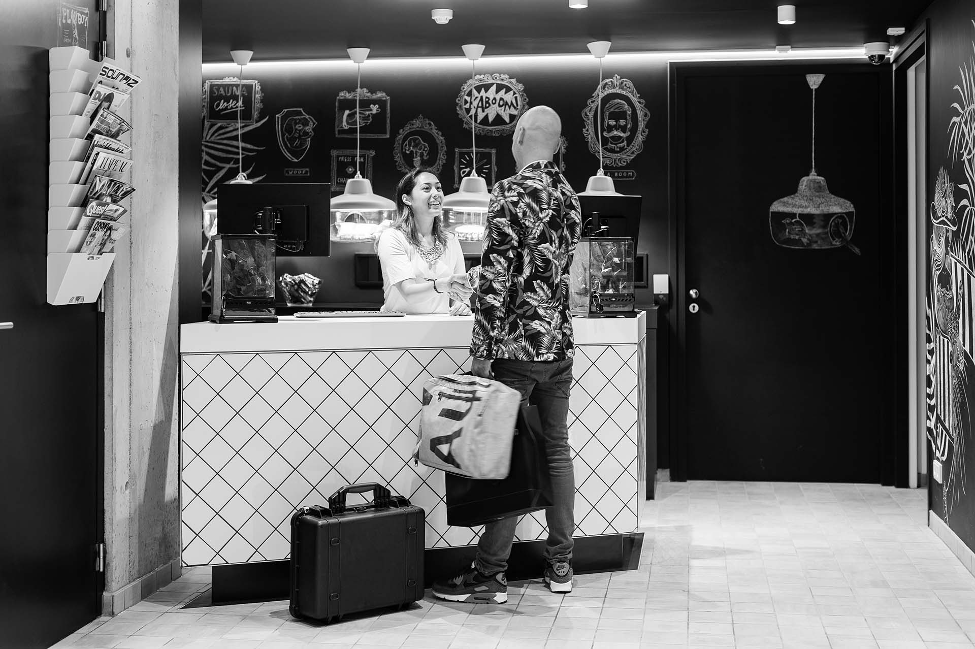 Receptioniste bij de receptie van het Kaboom Hotel ontvangt een gast, in zwart-wit | Kaboom Hotel
