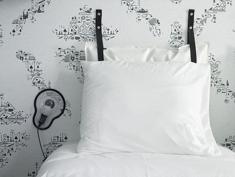 Bed with pillow at the head and lamp on one side | Kaboom Hotel