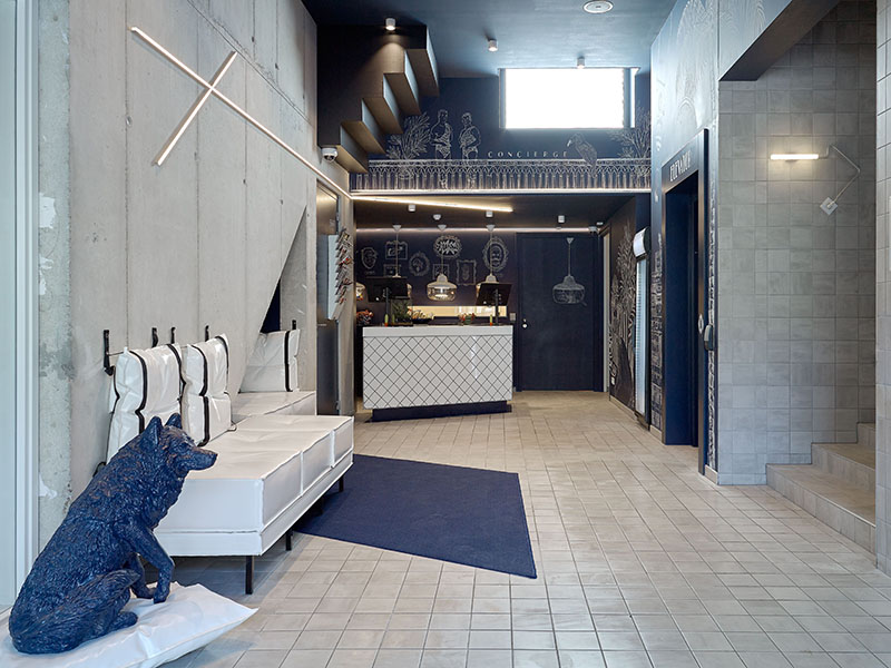 Lobby van Hotel Kaboom met blauwe hondenfiguur, witte banken en receptie | Kaboom Hotel