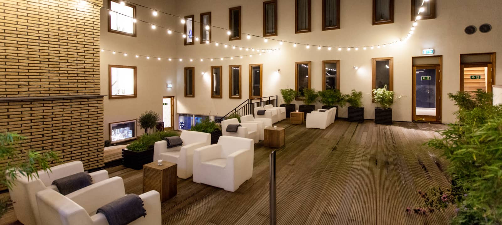 Internal patio of building with wooden terrace, white benches and plant decoration | Kaboom Hotel