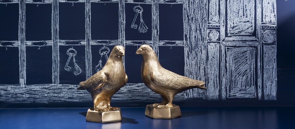 Two small gold bird figures on blue shelf and blue patterned wall | Kaboom Hotel