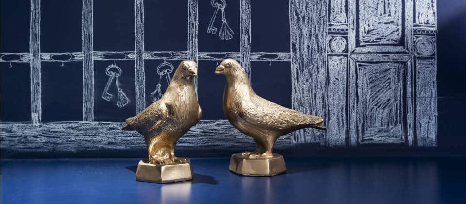 Twee kleine gouden vogelfiguren op blauwe plank en blauwe muur met patroon | Kaboom Hotel