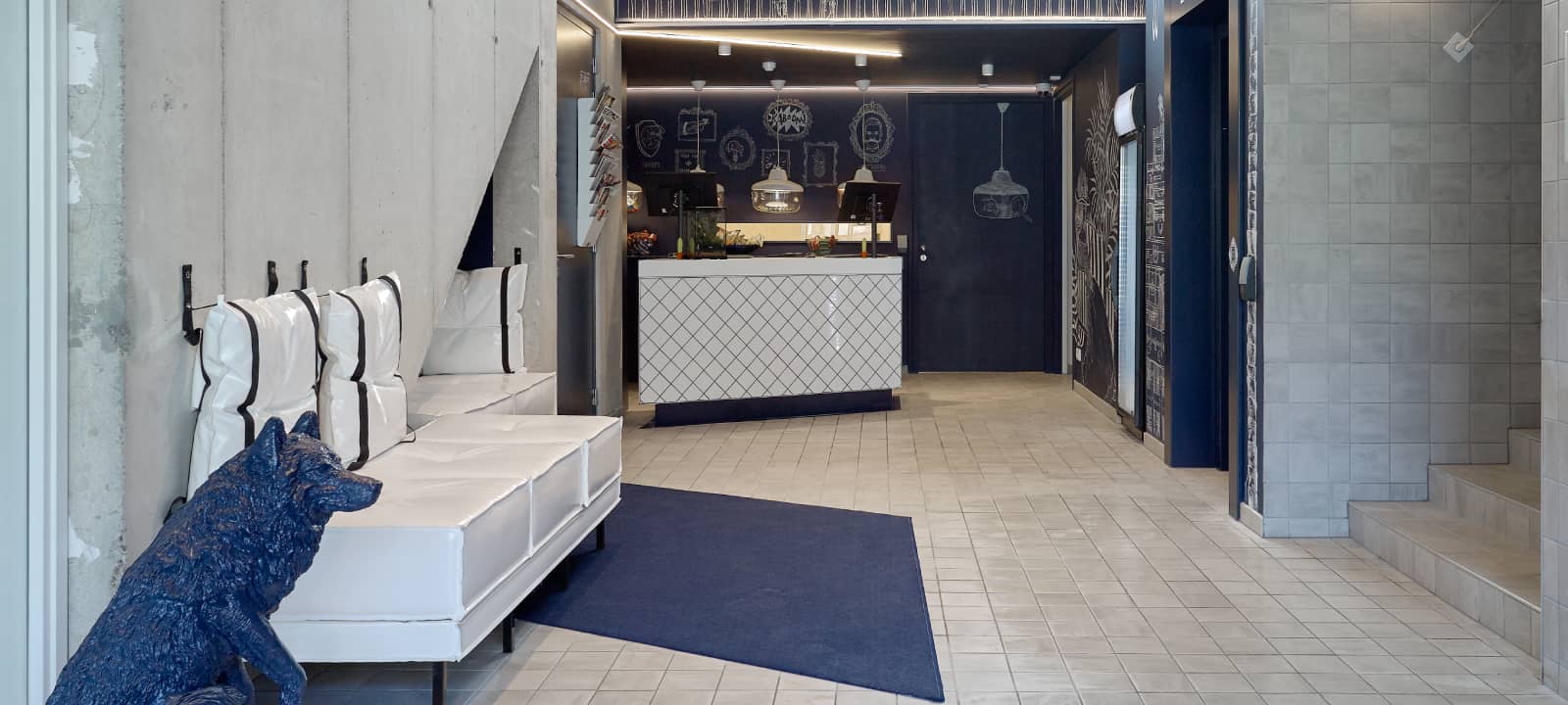 Lobby van Hotel Kaboom met blauw hondenfiguur, witte banken en receptie | Kaboom Hotel