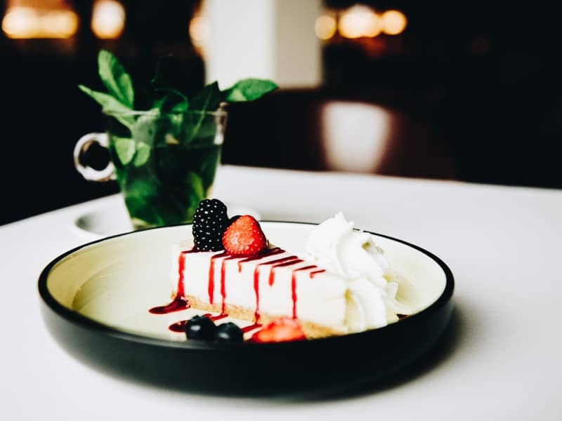 Schwarzer Teller mit einem Stück rotem Obstkuchen mit Kräutertee daneben | Kaboom-Hotel